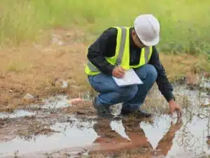 un professionista con un elmetto da lavoro sta ispezionando e prendendo appunti in una zona di scarico acqua per un'analisi ambientale.