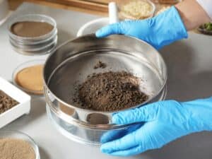 Un tecnico in guanti blu sta setacciando un campione di terreno, un passo chiave nell'analisi ambientale del suolo per valutare la qualità e la composizione del terreno.