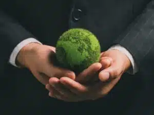 Un individuo in giacca e camicia tiene tra le mani un globo ricoperto di muschio, rappresentando il concetto di custodia e rispetto delle norme ambientali