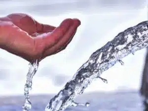 una mano aperta con il palmo verso l'alto che raccoglie l'acqua che sgorga da una fontana o una sorgente